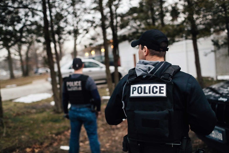 Unidentified men wearing "POLICE" vests stand outside a house.